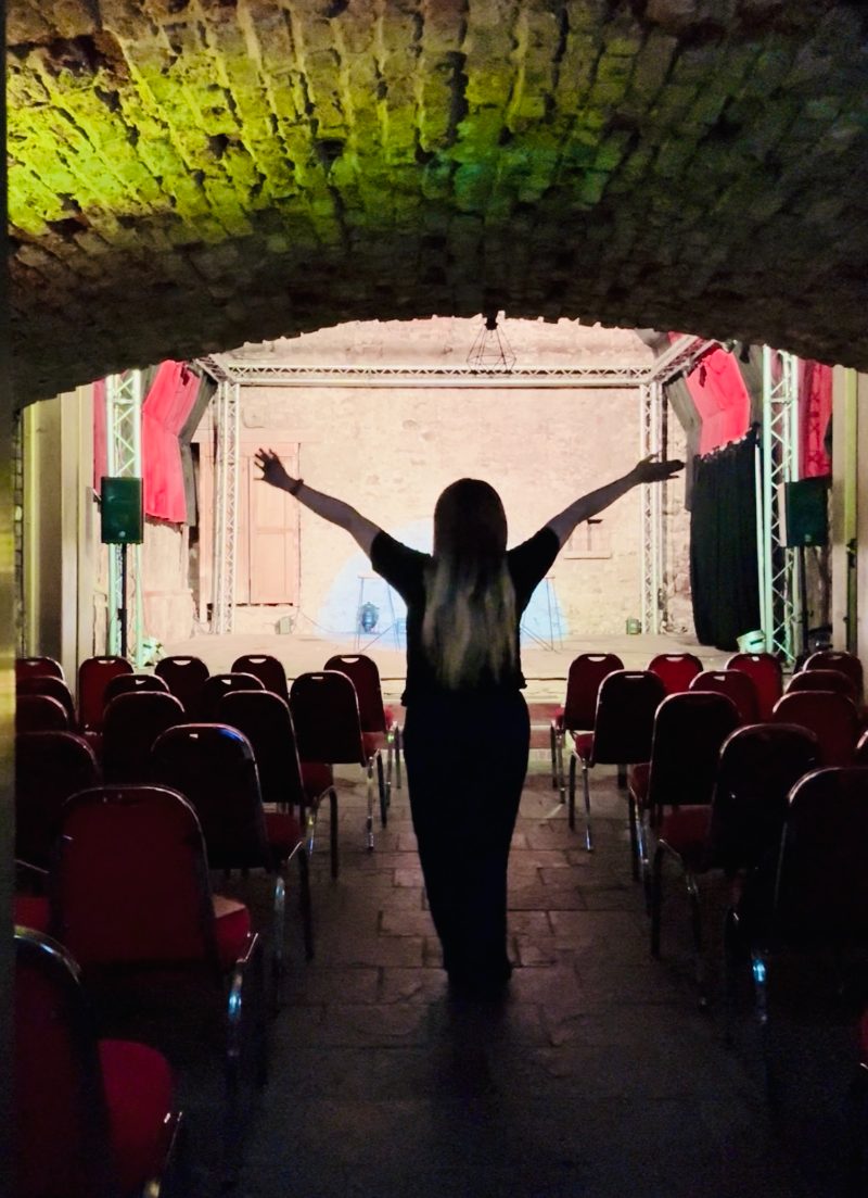Bilee J with arms raised before the stage in the vaulted room at the Caves