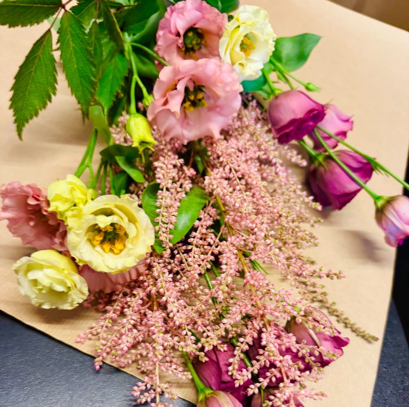 A bouquet of pink, cream, and plum flowers wrapped in brown paper